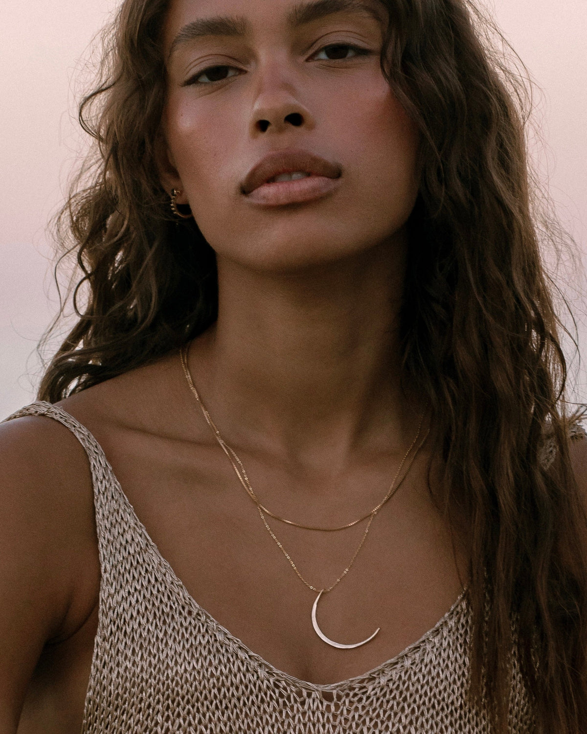 Model wearing layered gold necklaces with crescent moon pendant