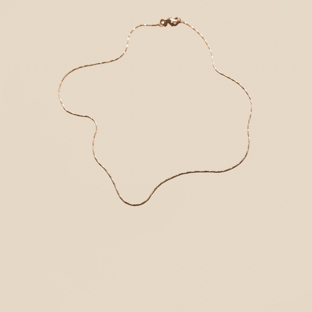 The Golden Hour Chain by LLUME Jewelry, an elegant 18k gold filled necklace, is displayed in an abstract wavy design against a beige background.