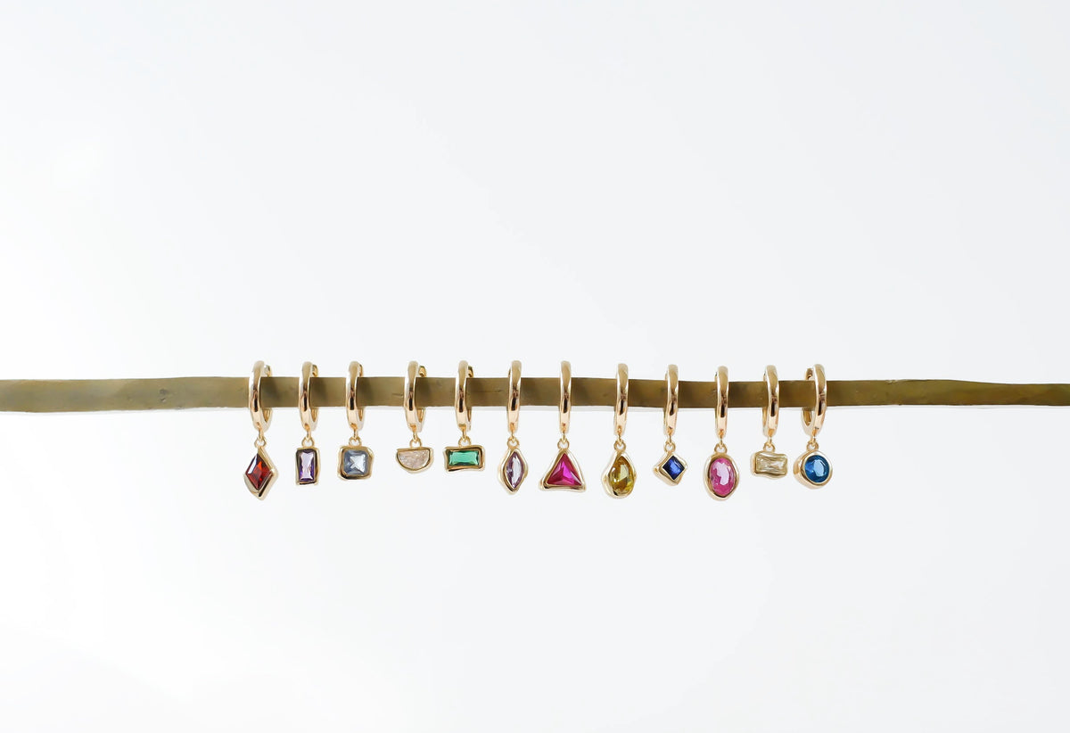 LLUME Jewelry's Birthstone Earrings feature ten gold-plated hoops, each with a unique gemstone charm, displayed on a gold rod—ideal for personalized gifts or birthstone jewelry.