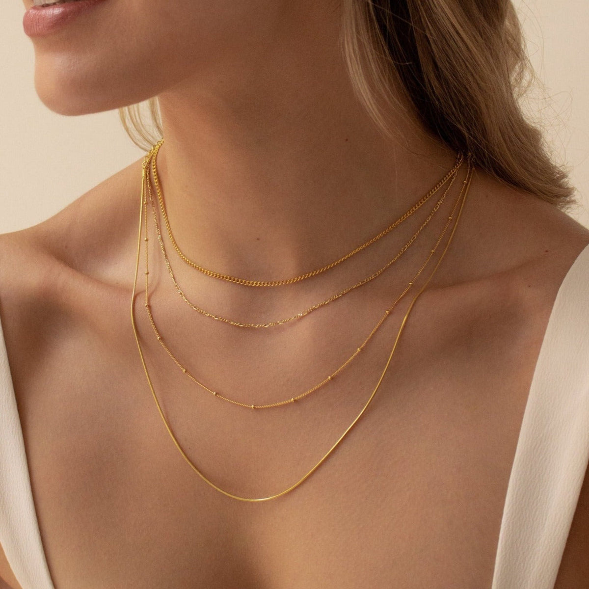 A woman wears layered essential gold chains in different lengths and styles across her neck and collarbone.