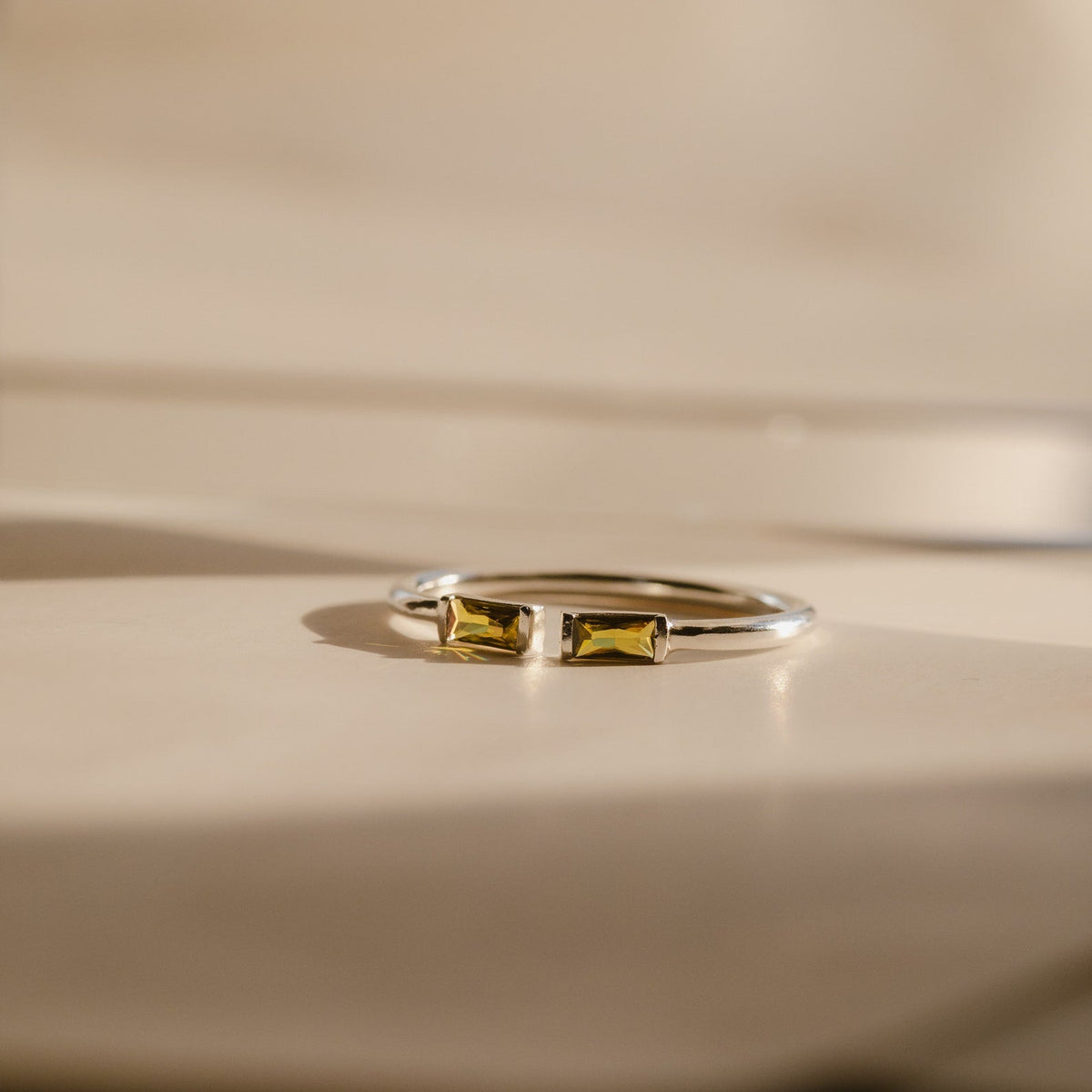 A Duo Baguette Birthstone Ring with two rectangular yellow stones sits on a beige surface, ideal for a personalized gift or displaying your chosen birthstones.