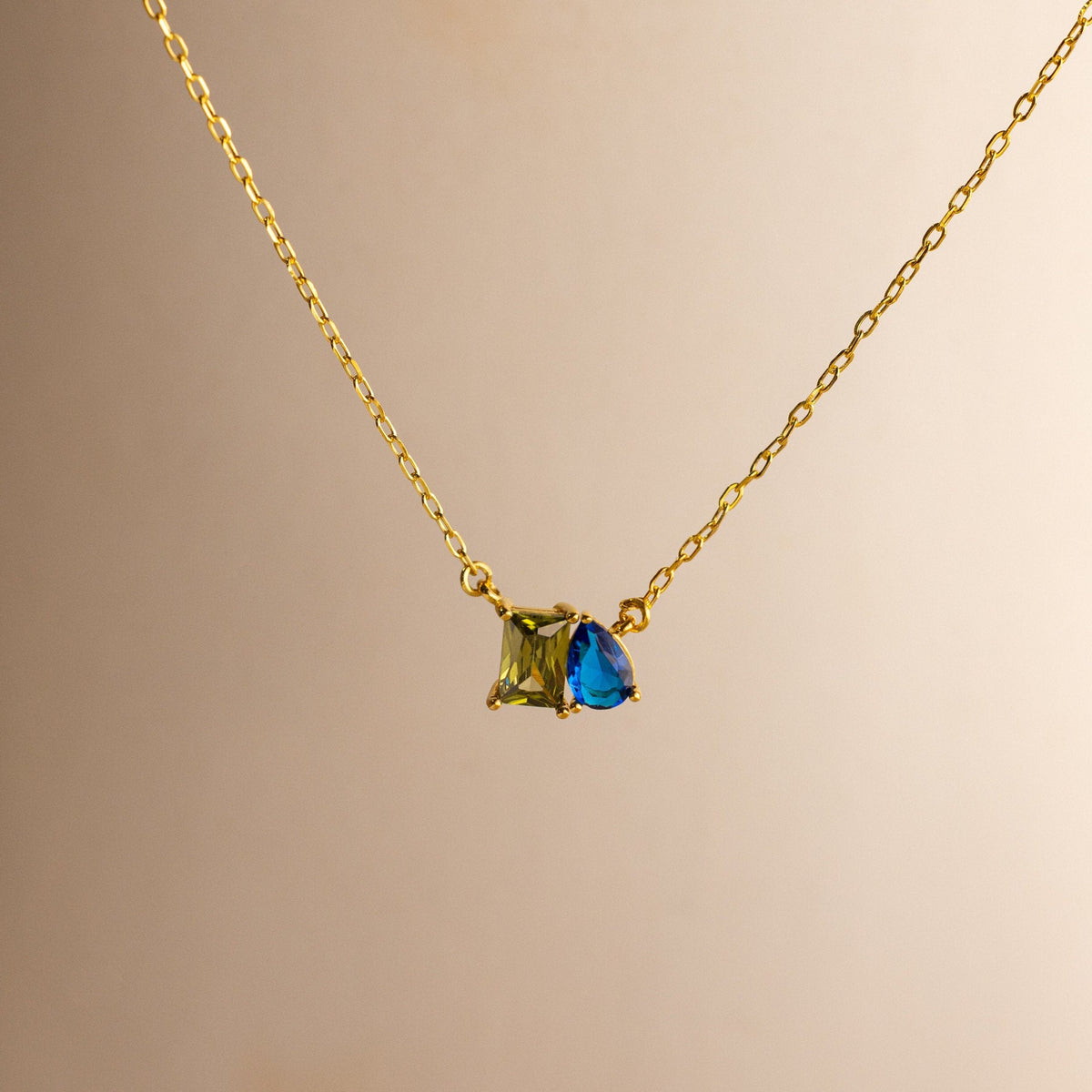 The Toi et Moi Birthstone Necklace showcases a green square-cut and blue teardrop-cut gemstone—ideal for custom birthstone jewelry lovers seeking a classic, personalized necklace. Styled on a neutral background for timeless appeal.