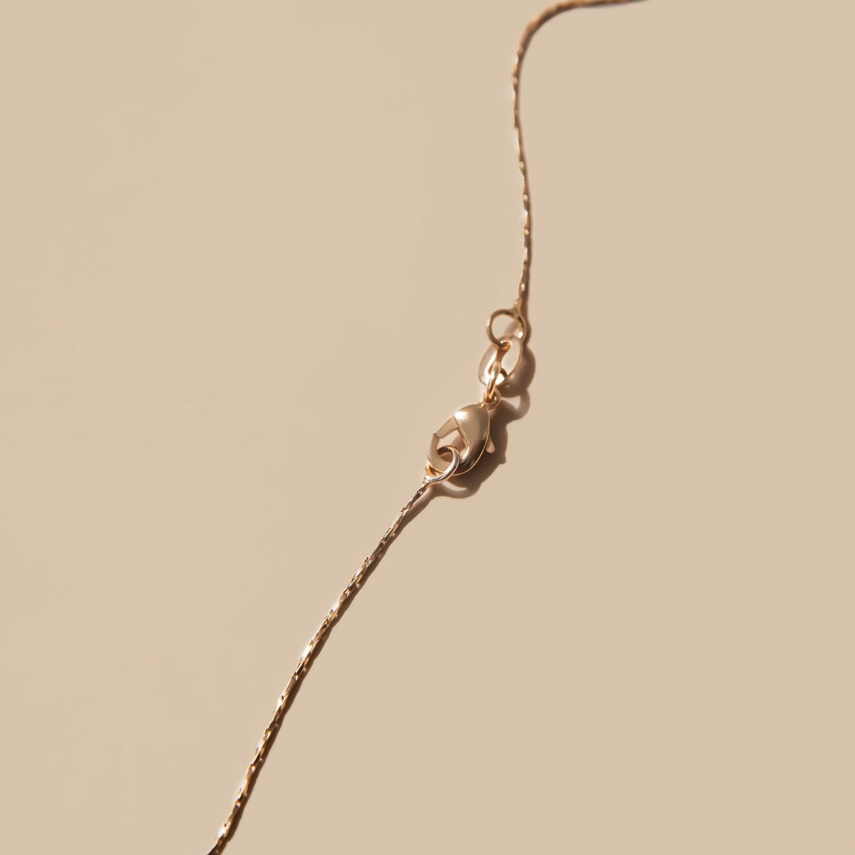 Close-up of the Golden Hour Chain by LLUME Jewelry, a delicate 18k gold-filled necklace with a lobster clasp, displayed on a soft beige background.