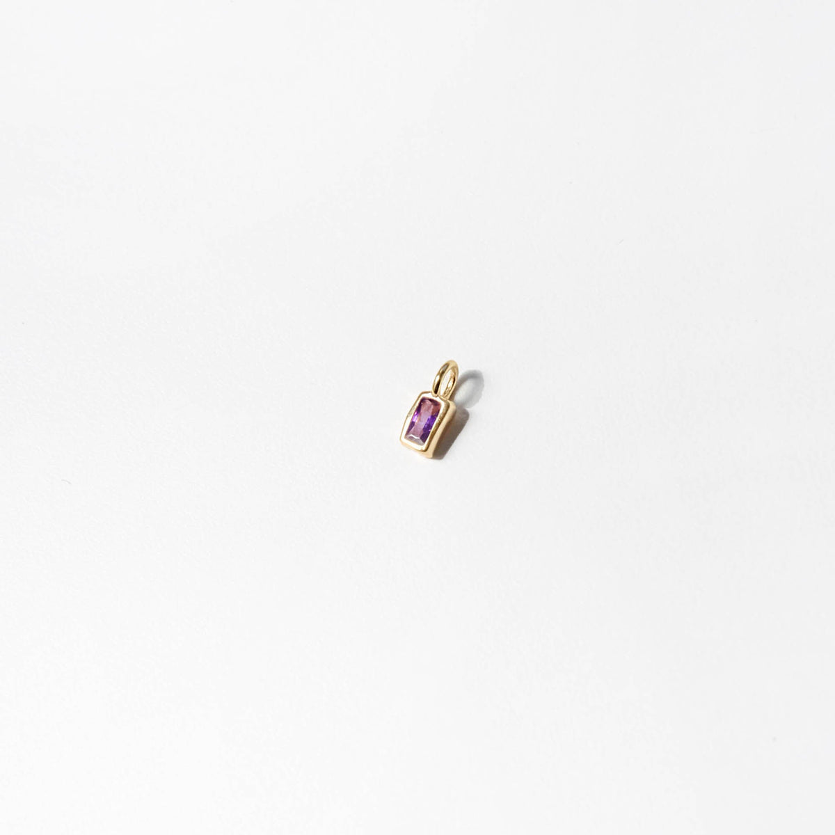 The LLUME Jewelry Build a Birthstone Necklace features a small rectangular gold pendant with a central purple gemstone, elegantly photographed on a plain white background.