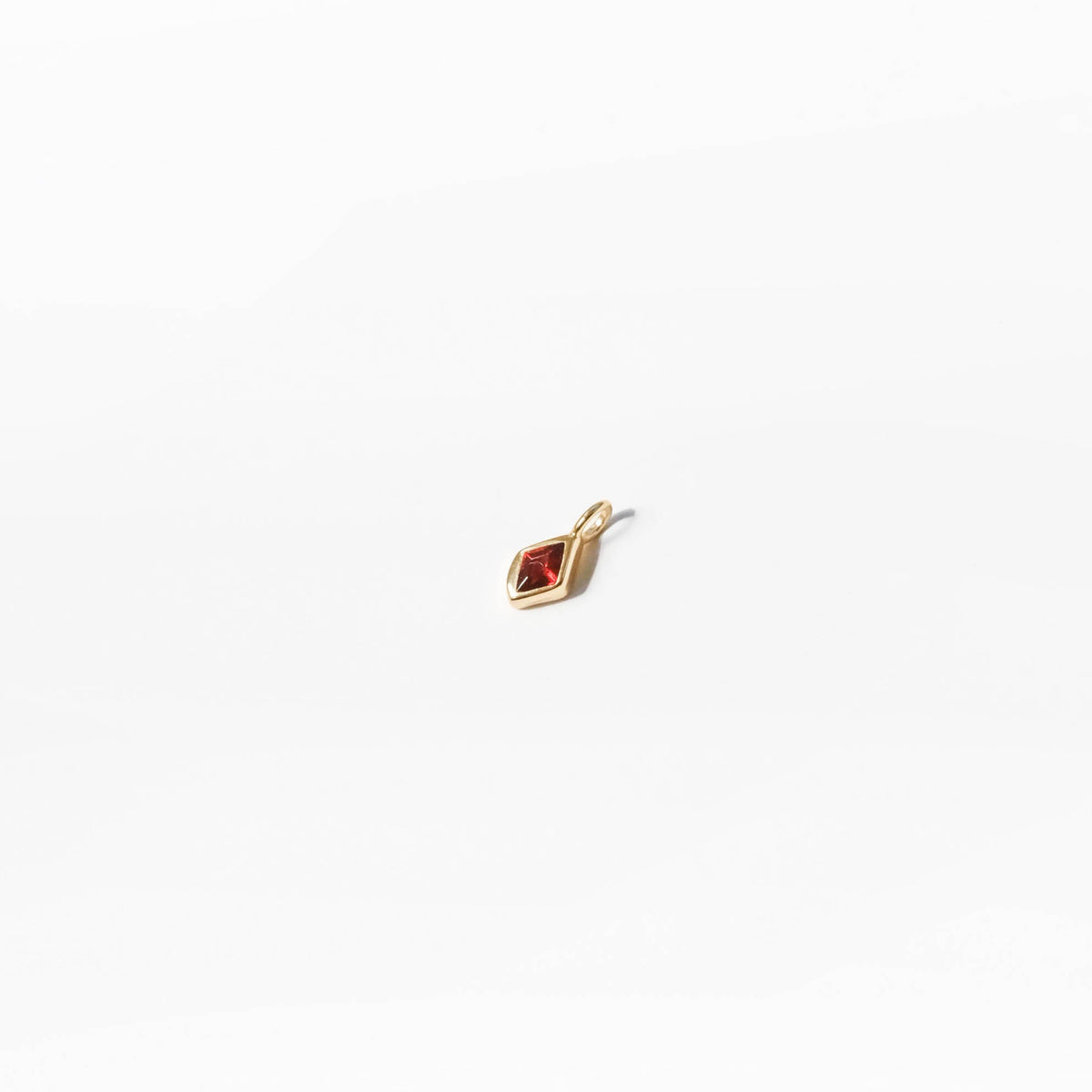 The Build a Birthstone Necklace by LLUME Jewelry features a small gold plated diamond-shaped charm with a red center gemstone, ideal for creating a custom or unique birthstone necklace. Shown on a plain white background.