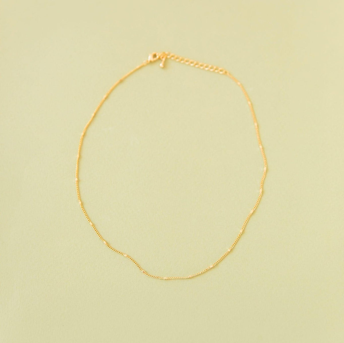 The Linden Chain by LLUME Jewelry, crafted in 18K gold-plated metal with an adjustable clasp and extension, is displayed flat on a pale yellow background.