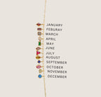 The LLUME Jewelry Build a Birthstone Necklace features a gold chain with twelve gold-plated charms, each displaying a unique birthstone for every month, aligned vertically beside the months January to December in black text.