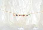 The LLUME Jewelry Build a Birthstone Necklace, featuring a delicate gold chain with customizable colorful gemstone and gold plated charms, is displayed against a softly lit white fabric background.