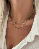 Model wearing two layered gold paperclip chain necklaces of different lengths over a white linen top