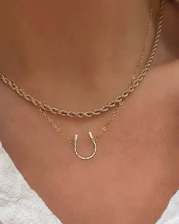 Model wearing layered gold horseshoe necklace with rope chain