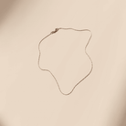 The Golden Hour Chain by LLUME Jewelry is a delicate 18k gold filled necklace with a thin chain and small clasp, displayed in a wavy shape on a plain light beige background.
