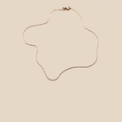 The Golden Hour Chain by LLUME Jewelry, an elegant 18k gold filled necklace, is displayed in an abstract wavy design against a beige background.