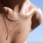 A woman's neck and shoulders are shown in sunlight, wearing the LLUME Jewelry Taylor Daily Set—featuring a delicate necklace and small rectangular Taylor Pendant—with a clear blue sky in the background.