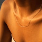 Close-up of a person wearing the LLUME Jewelry Golden Hour Chain, an 18k gold filled necklace that catches warm sunlight on their neck and shoulders. They’re dressed in a light top with thin straps.