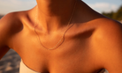 A close-up of a sunlit neck and collarbone adorned with LLUME Jewelry’s Golden Hour Chain, an elegant 18k gold filled necklace, the delicate contours glowing against a softly blurred outdoor background.