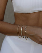 Model wearing three stacked gold chain bracelets on wrist
