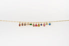 The Build a Birthstone Necklace by LLUME Jewelry features a gold chain with eleven unique, gold-plated gemstone charms in different shapes and settings, showcased against a plain white background.