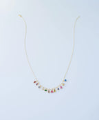 The LLUME Jewelry Build a Birthstone Necklace features gold-plated custom charms and small, colorful birthstone gems in various shapes, evenly spaced along the lower chain, displayed on a plain light background.