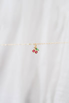 The LLUME Jewelry Build a Charm Necklace features a delicate gold chain with a cherry pendant of two red beads and green leaves, perfect for personalizing your necklace collection. Shown on a soft white background.