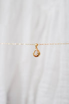 The LLUME Jewelry Build a Charm Necklace features a delicate gold chain with a teardrop clear gemstone pendant and gold-filled charms, beautifully displayed on a soft white background.