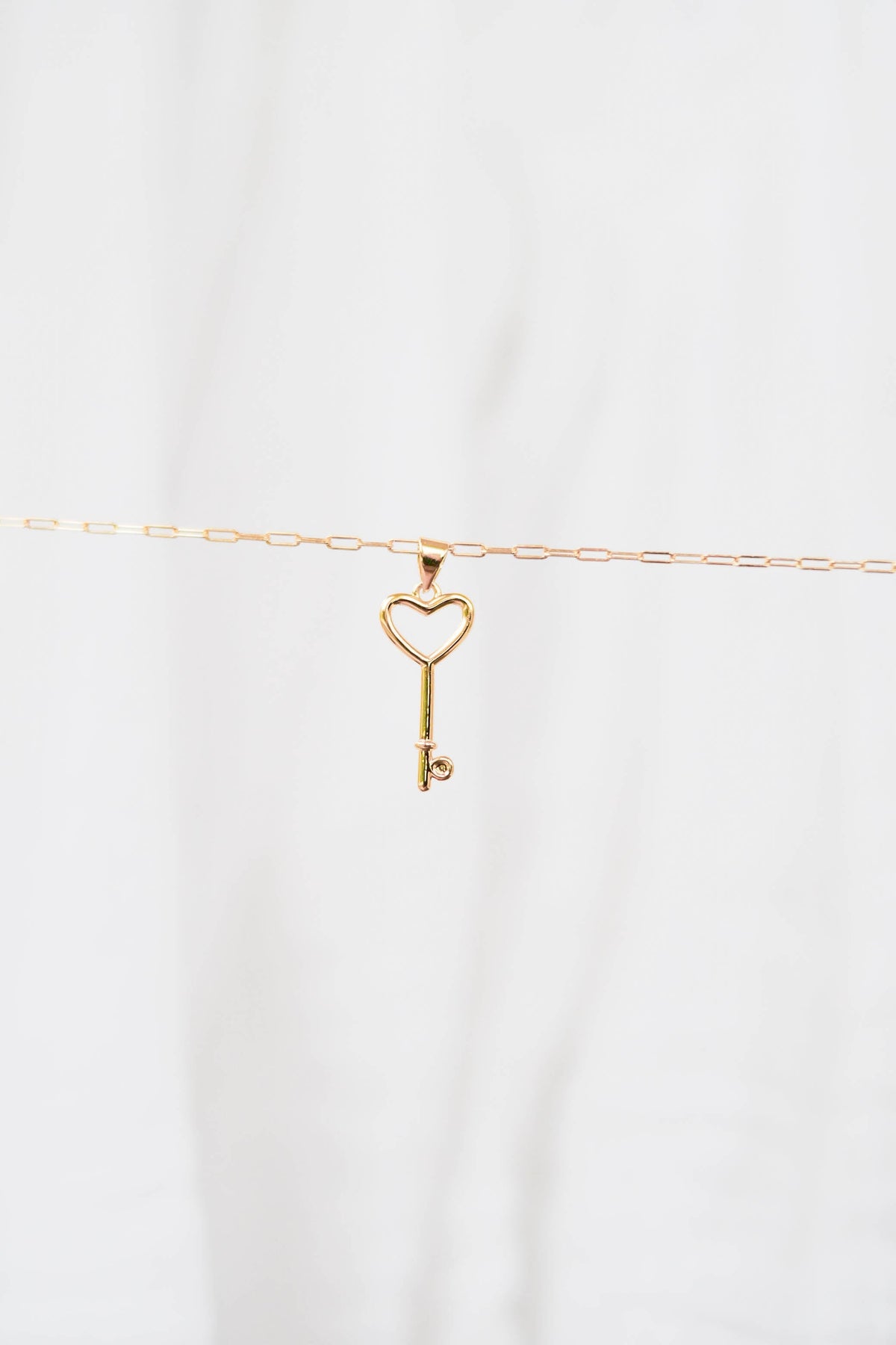 The LLUME Jewelry Build a Charm Necklace features a delicate gold chain with a heart-topped key pendant, perfect for personalization. Shown on a plain white background.