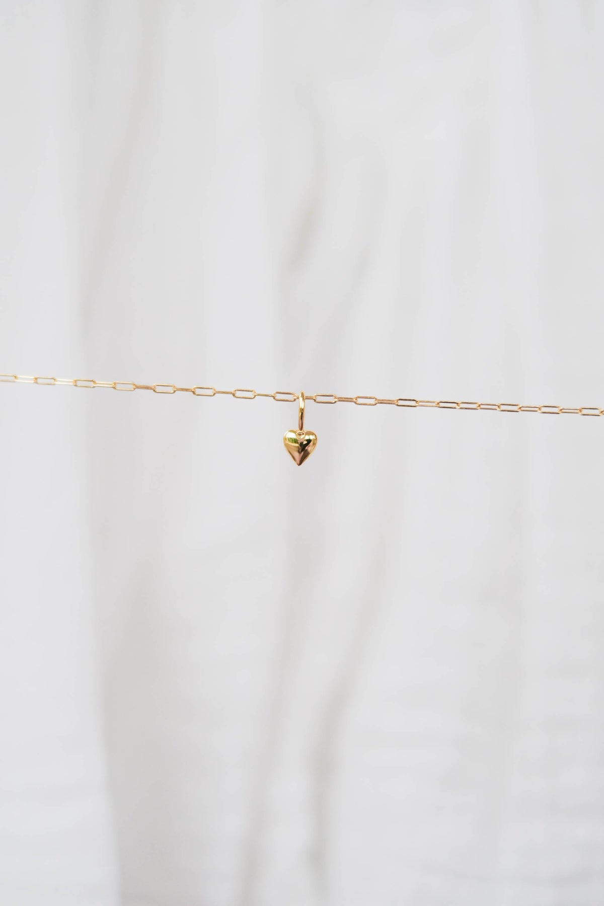 The LLUME Jewelry Build a Charm Necklace features a delicate gold chain with a small heart pendant—perfect for layering or personalizing with your favorite gold-filled charms.