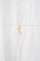 The LLUME Jewelry Build a Charm Necklace features a delicate gold chain with a cursive "mama" pendant and gold-filled charms, displayed on a soft white background—ideal for personalizing or creating your unique charm necklace.