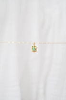 The LLUME Jewelry Build a Charm Necklace features a delicate gold chain with a small rectangular pendant set with a green gemstone, perfect for personalizing your jewelry. Shown against a soft white background.