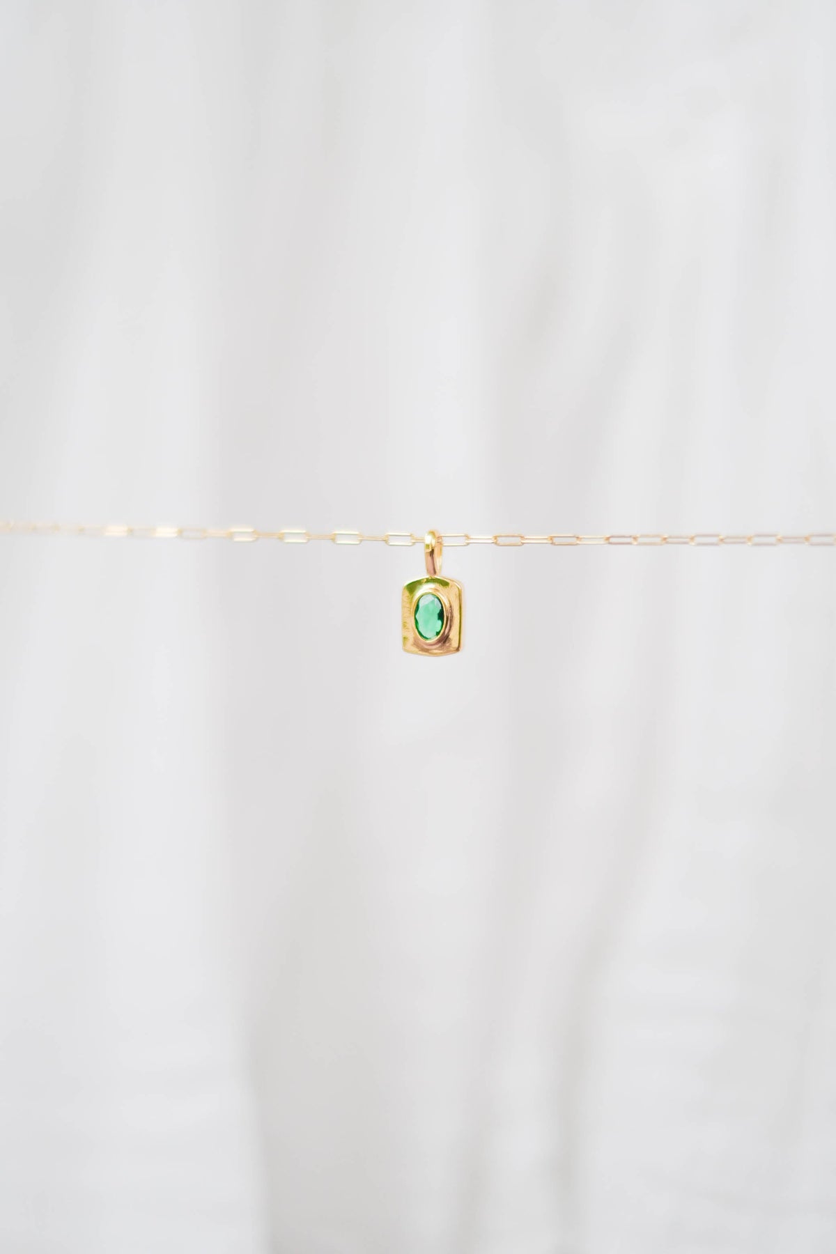 The LLUME Jewelry Build a Charm Necklace features a delicate gold chain with a small rectangular pendant set with a green gemstone, perfect for personalizing your jewelry. Shown against a soft white background.