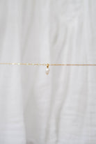 The Build a Charm Necklace by LLUME Jewelry features a delicate gold-filled chain with a single white pearl pendant—ideal for layering or adding your favorite charms. Displayed elegantly against soft white fabric.