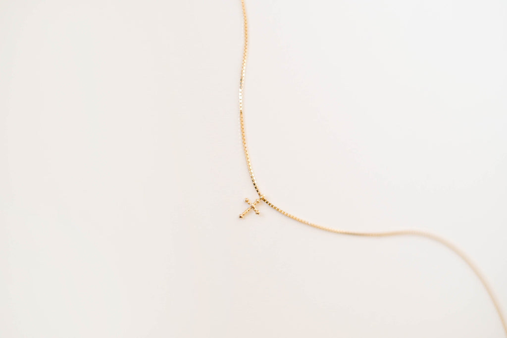 The LLUME Jewelry Cross Necklace showcases a dainty gold-plated chain with a cross pendant, elegantly displayed against a simple light background.