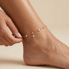 Hand holding the Elodie gold anklet with crystal clovers, round crystal stations and one dangling clover