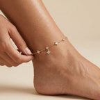 Hand holding the Elodie gold anklet with crystal clovers, round crystal stations and one dangling clover