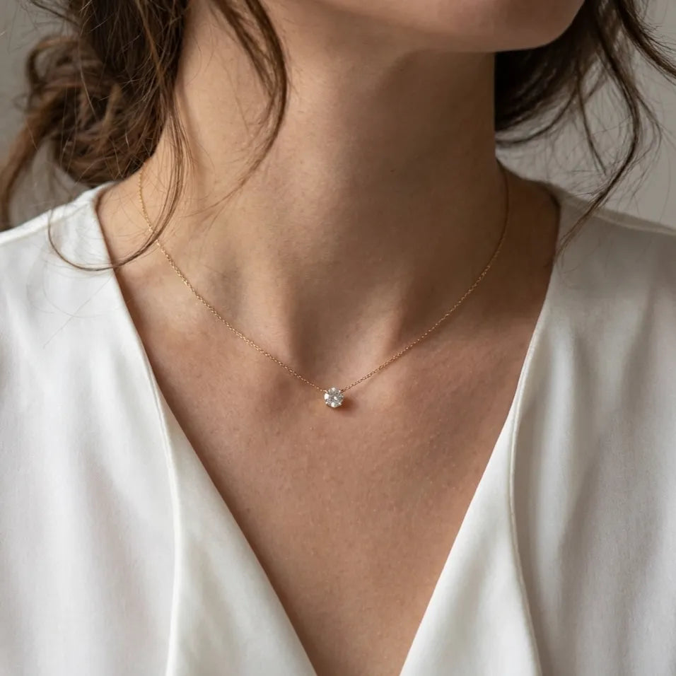 Woman in a white blouse wearing the Lora gold necklace with a single round crystal at the throat