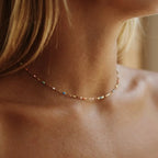 Woman wearing the Celeste gold chain choker dotted with tiny multicolored enamel beads at the throat