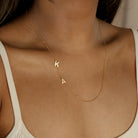 The Sideways Initial Necklace features gold K and A letter charms, shown on a person in a cream-colored top—making it the perfect personalized Christmas gift.
