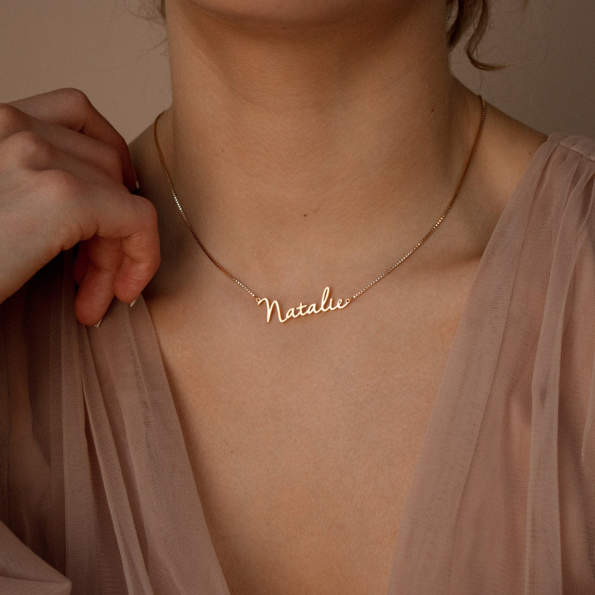 A woman wears the Callie Box Chain Name Necklace in 18K Gold, personalized with the name Natalie in cursive script and featuring a customizable charm.