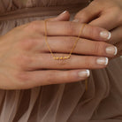 Close-up of hands holding the Tiny Summer Name Necklace in a delicate font with the name "anna." The wearer is dressed in a sheer beige dress, highlighting the necklace’s elegant and personalized design.