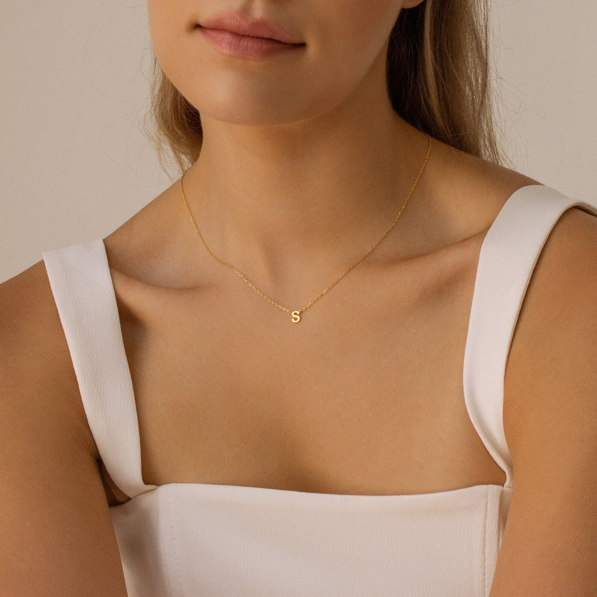 A woman wears the Alice Dainty Initial Necklace, a gold personalized piece featuring a small letter S pendant—an elegant gift idea for Christmas.