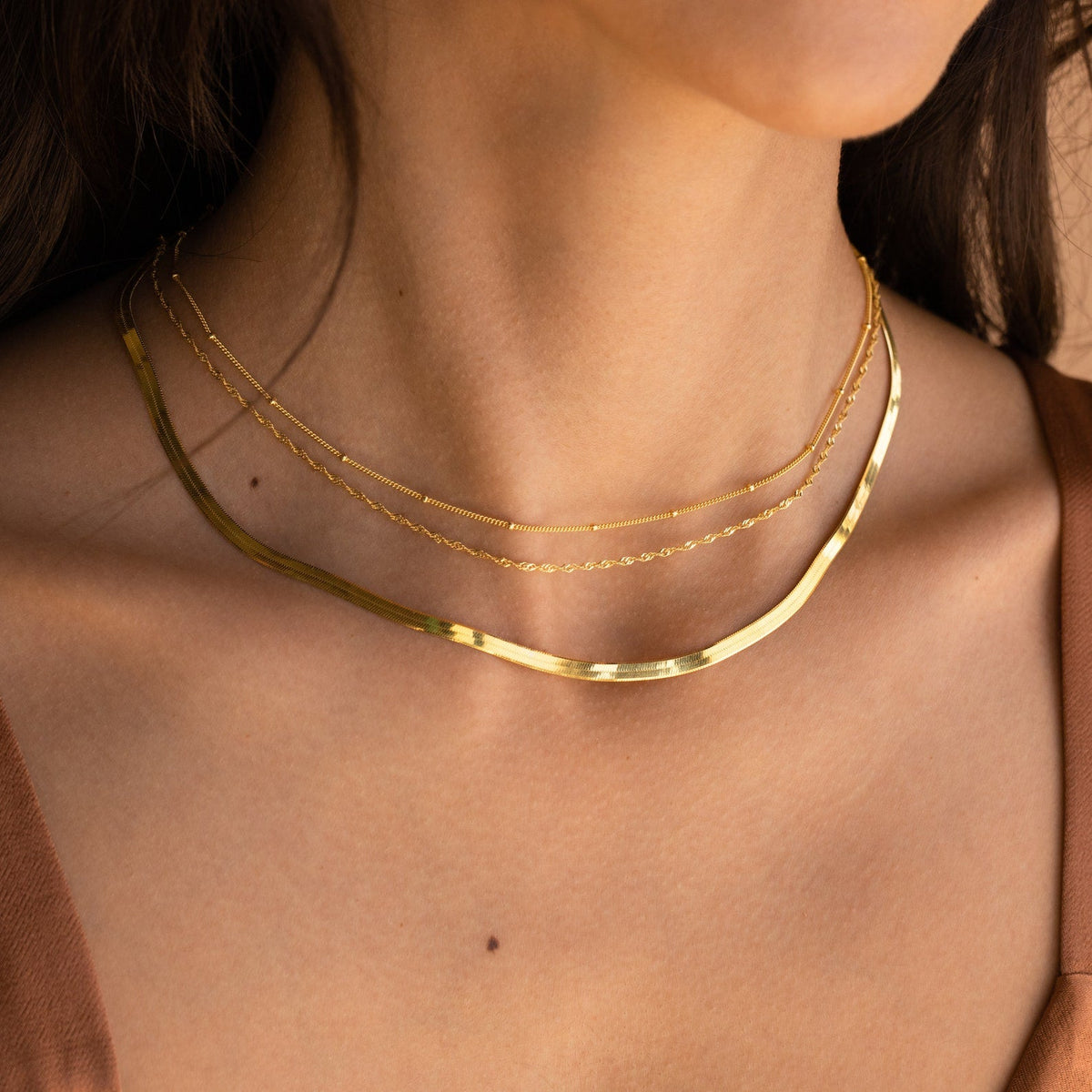 Close-up of a woman’s neck wearing layered gold chains, including a thick snake chain and two delicate styles.