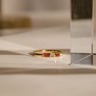 The Duo Baguette Birthstone Ring, featuring two rectangular red stones, rests on a white surface in gentle sunlight—a beautiful choice for a personalized gift.
