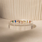 Five handcrafted rings with vibrant rectangular gemstones are displayed on a clear stand in soft light, highlighting the Duo Marquise Baguette Ring for a personalized gemstone jewelry touch.