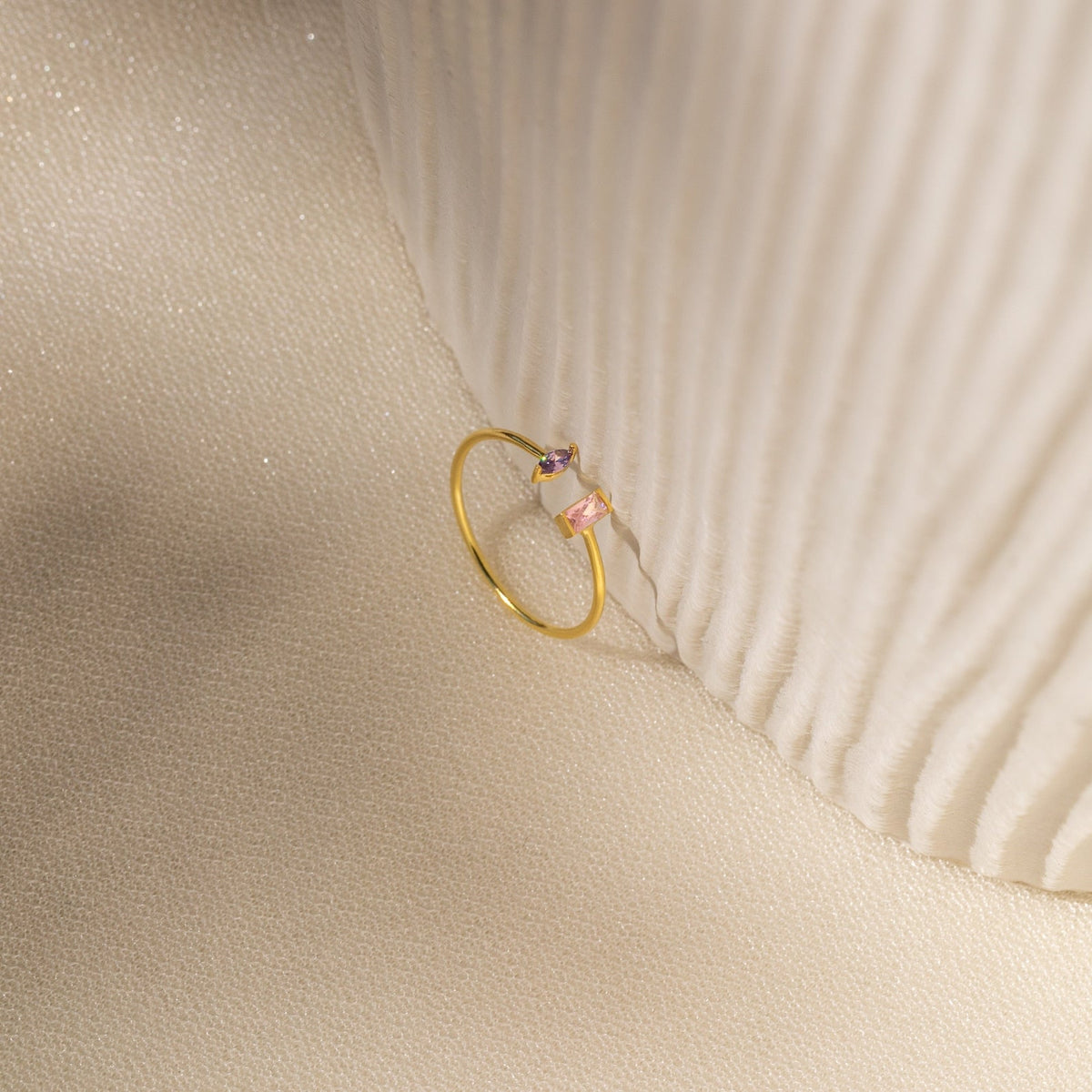 The Duo Marquise Baguette Ring gleams atop a textured cream fabric, highlighting the elegance and craftsmanship of this handmade jewelry piece.