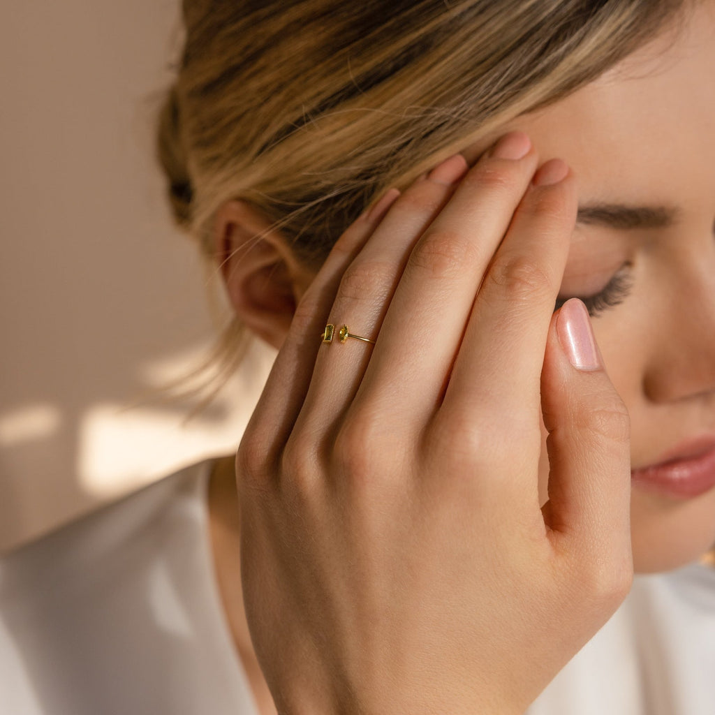 A woman with her eyes closed touches her forehead, elegantly showcasing the Duo Marquise Baguette Ring under soft lighting.