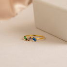 Cluster Baguette Birthstone Ring in Rose Gold, featuring green, purple, clear, and blue gemstones, displayed next to a textured cream-colored box.