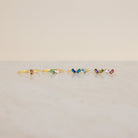 Five Cluster Baguette Birthstone Rings with colorful gemstones are arranged in a row on a light marble surface against a beige background, perfect as birthstone or personalized statement rings.