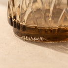 The Tiny Dream Name Necklace, featuring "Harper" in delicate cursive, rests at the base of a textured glass container.