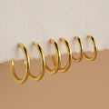 Six gold Mini Bold Hoops from our collection hang on the edge of a white textured surface, showcasing their varying sizes and timeless style.