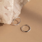 The Mini Bold Hoops Set from our collection rests on a beige surface beside a textured white crystal.