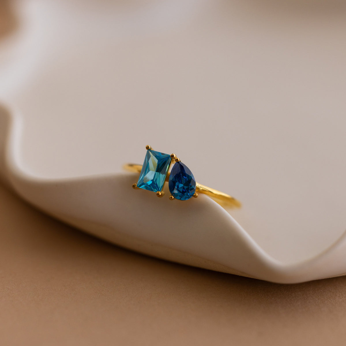 Toi et Moi Birthstone Ring in Rose Gold featuring two blue gemstones—one square, one teardrop—set on a wavy dish. Customizable and perfect as a unique Christmas gift.